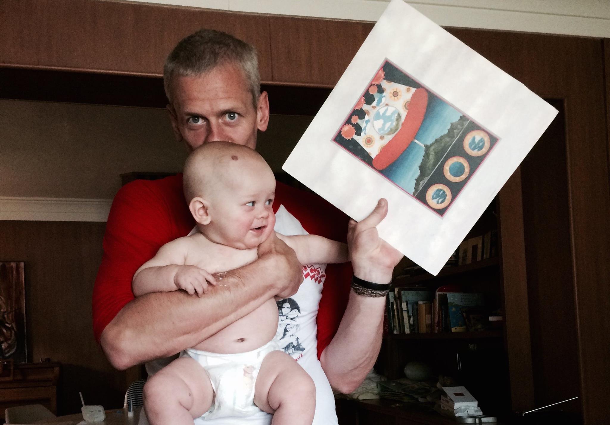 Patrick Tape Fleming holding his son Nilsson and a Copy of Dusk at Cubist Castle by the Olivia Tremor Control