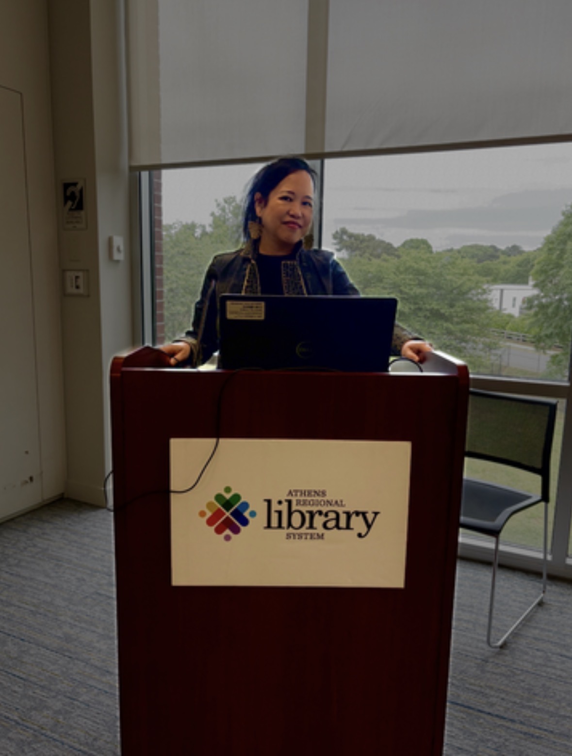 Silvia Passiflora, Southern Gothic Folk poet-songwriter, stands at a wooden lectern bearing the Athens Regional Library System seal during the Community Poetry Open Mic at the Athens-Clarke County Regional Library, Athens, Georgia, April 19, 2026.