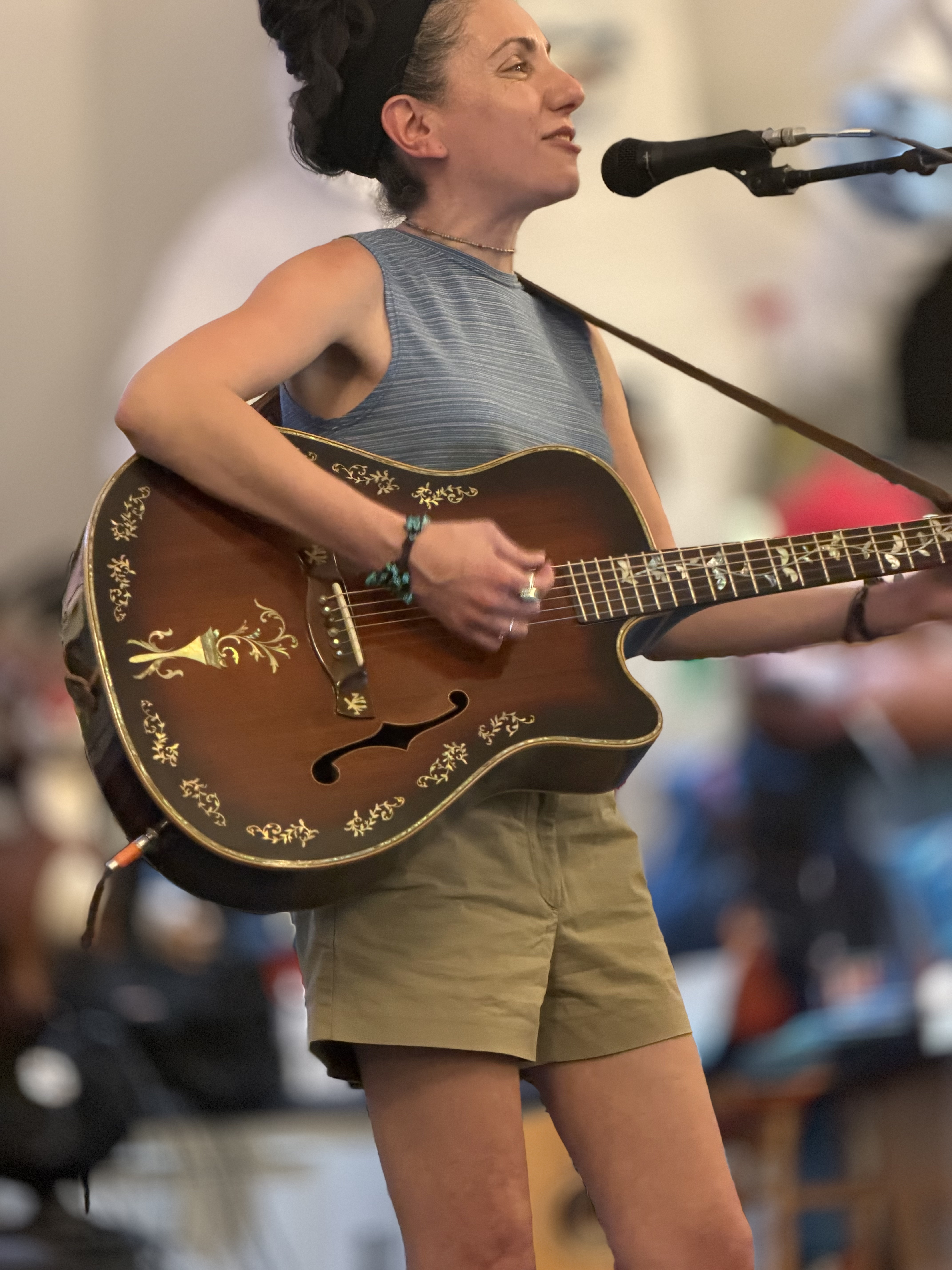 Laura standing behind a microphone, playing her guitar and singing