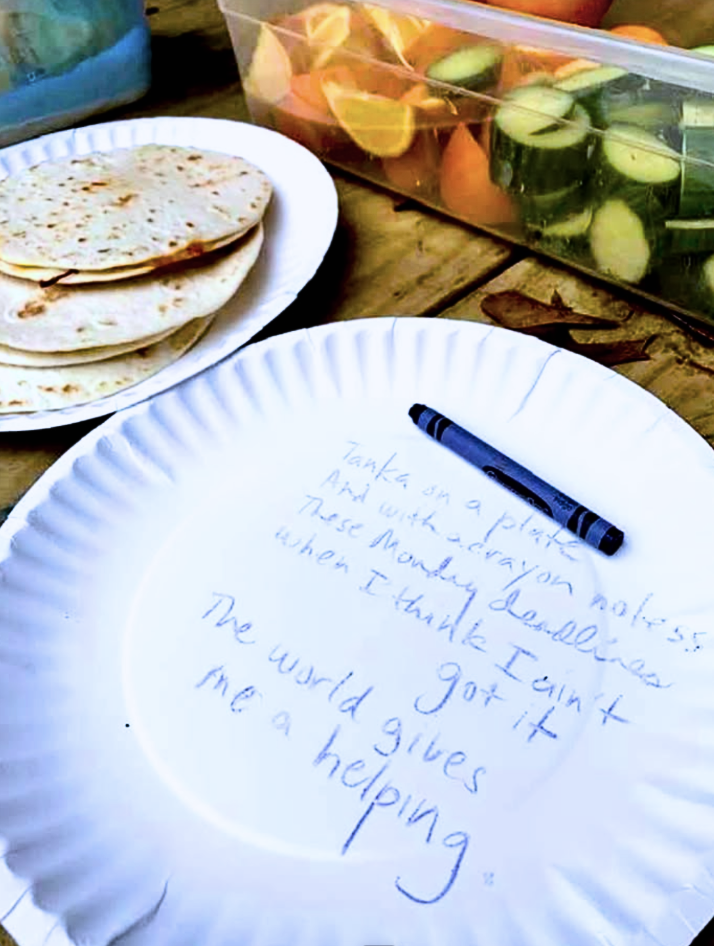 Scriptaluna — a tanka poem written in blue crayon on a paper plate by Silvia Passiflora, resting beside flour tortillas and sliced vegetables, written between lunch service and dishes.