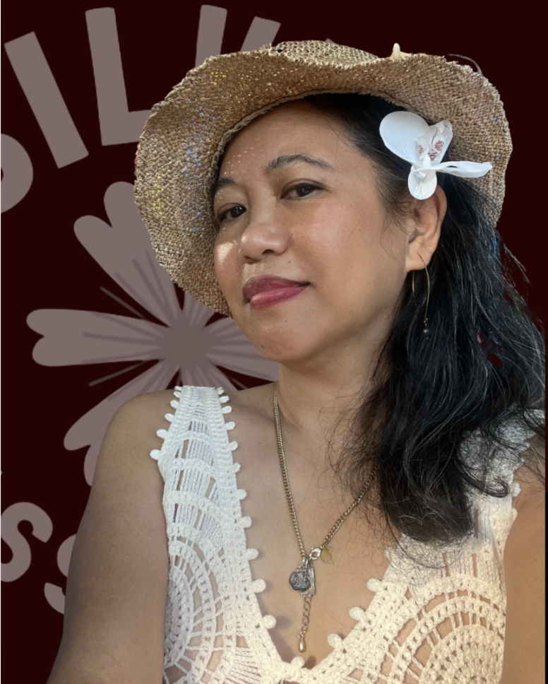Silvia Passiflora, a Southern Gothic Folk poet-songwriter. Silvia Passiflora wearing a gold glittery straw hat with a white orchid tucked behind her ear, a white crochet top, and gold hoop earrings, against a deep burgundy background featuring the Silvia Passiflora logo. She is looking slightly off camera with a warm, composed expression. 🌸