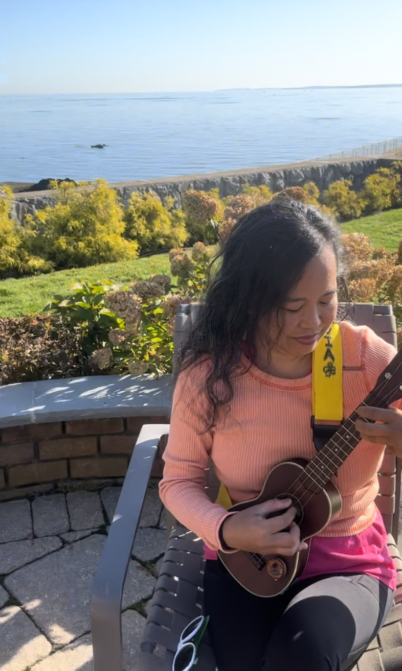 Silvia Passiflora playing an ukulele overlooking the ocean — searching, in practice.