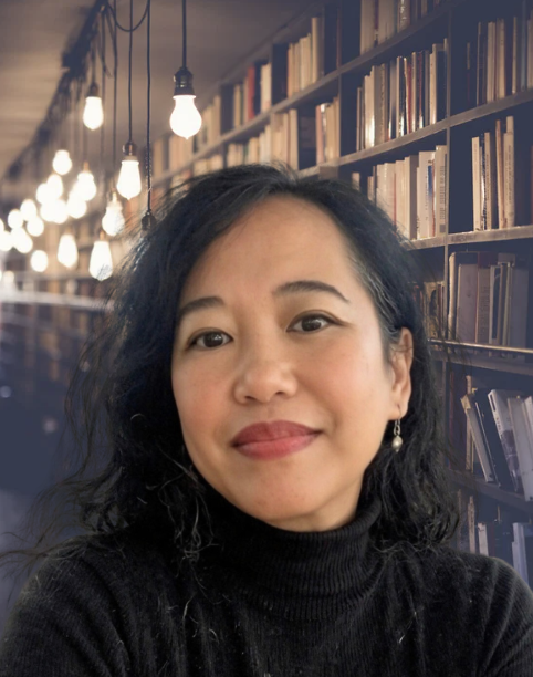 Silvia Passiflora, Southern Gothic Folk poet-songwriter wearing a black turtleneck facing the camera in a private library with pendant lights.
