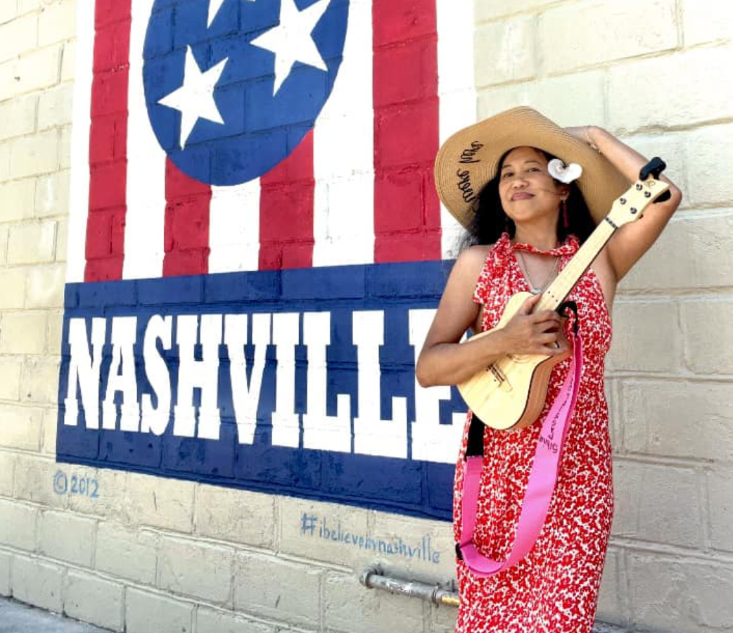 Silvia Passiflora, Southern Gothic Folk poet-songwriter, holding a ukulele in front of a Nashville mural featuring the Tennessee flag