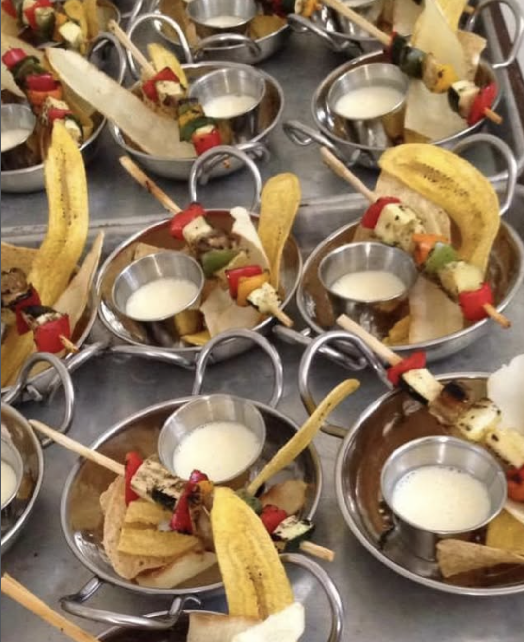Scriptaluna — Word of Mouth Cooking Club catering, stainless steel balti bowls each plated with a grilled vegetable skewer, tostones, and a coconut dipping sauce.