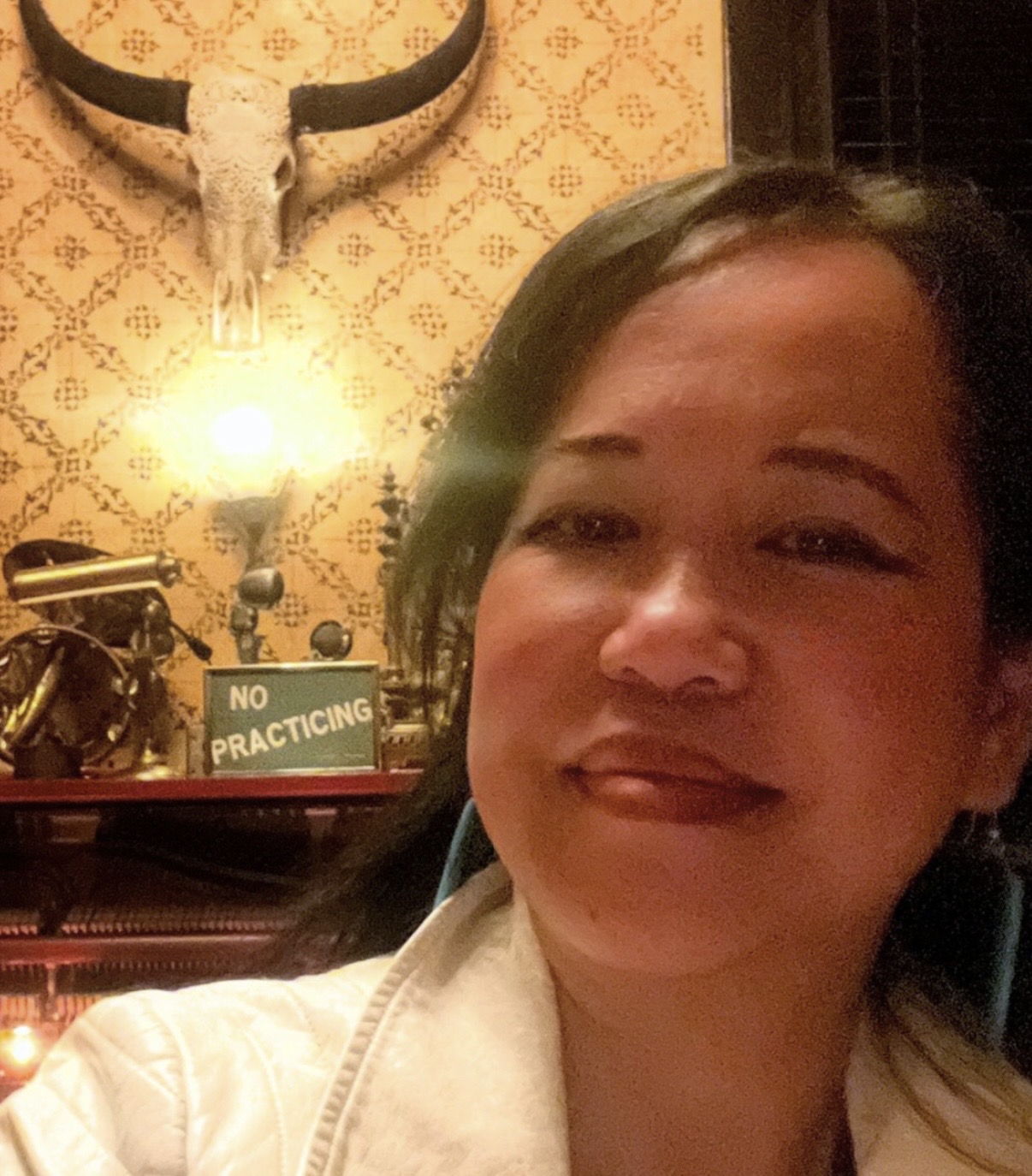 Silvia Passiflora, Southern Gothic Folk poet-songwriter and publisher of Scritpaluna LLC against a vintage wallpaper and steer's head display.