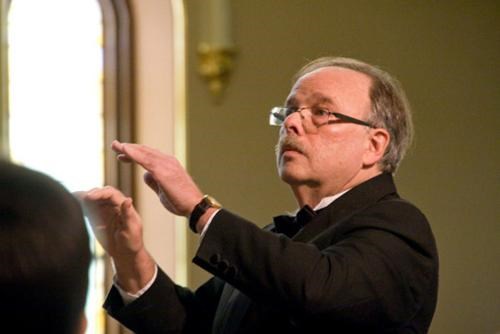 Bruce Borton, a white man with glasses and a mustache, with both hands raised to conduct