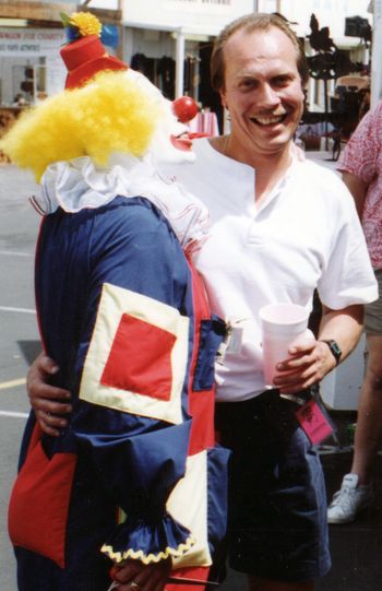 A guy in white pancake makeup, with a big, red nose & yellow hair and some clown.
