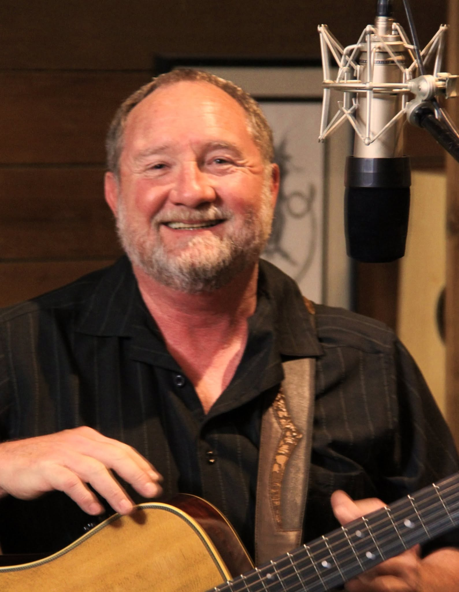 Bill smiling with his guitar beside a studio microphone