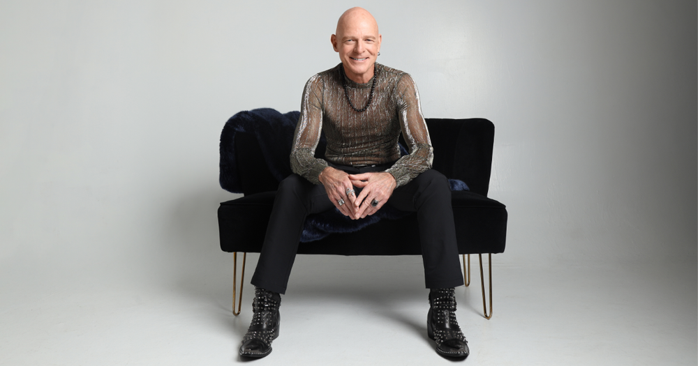 Jim Dix seated on a black couch in a studio portrait.