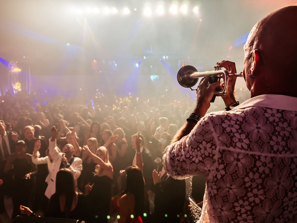 Jim Dix playing trumpet on stage, seen from behind, facing a large cheering audience