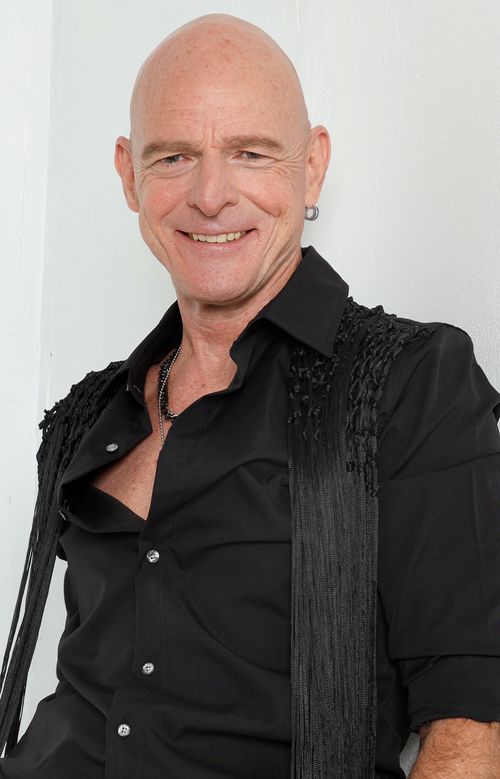 Portrait of musician Jim Dix smiling, wearing a black shirt against a white background.