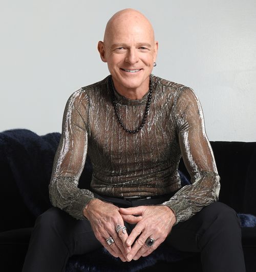 Jim Dix smiling in sheer metallic shirt on black couch
