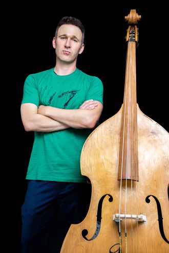 Joe Belson standing beside his upright bass, photographed by Bryon Malik.