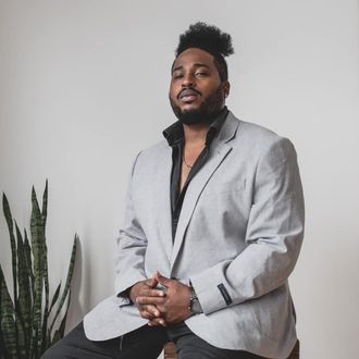 A portrait picture of Atryp wearing a sport jacket and collared shirt.  There is a plant next to him.
