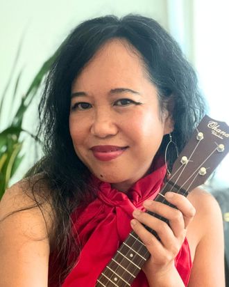 Silvia Passiflora, Southern Gothic Folk poet-songwriter, in a close portrait holding her Ohana ukulele with a red scarf tied at her neck, looking directly into the camera. 