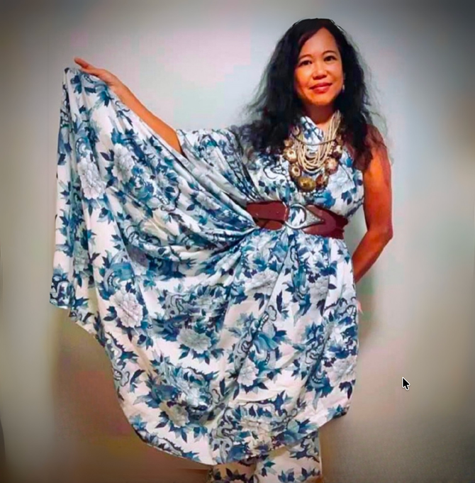 Silvia Passiflora, Southern Gothic Folk poet-songwriter wearing a blue and white floral belted  gown and shell necklaces. 