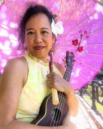 Silvia Passiflora, Southern Gothic Folk poet-songwriter, holding an ukulele beneath a vibrant pink parasol with a white flower in her hair, in a sunlit garden setting. 