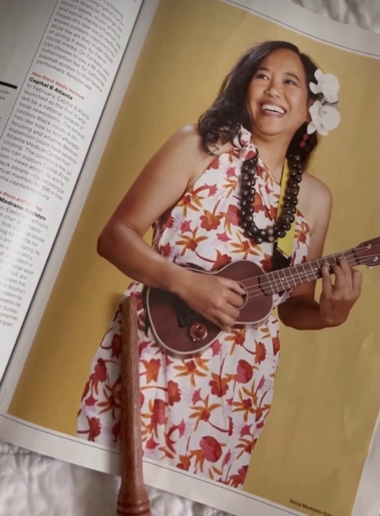 Silvia Passiflora Southern Gothic Folk poet-songwriter playing ukulele, pomegrante printed dress and island beaded necklace, flowers in her hair.
