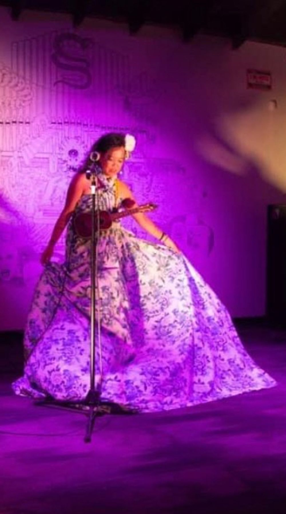 Silvia Passiflora, Southern Gothic Folk poet-songwriter, performing on stage in a sweeping blue and white floral gown under purple stage lighting, playing an ukulele, taking a bow