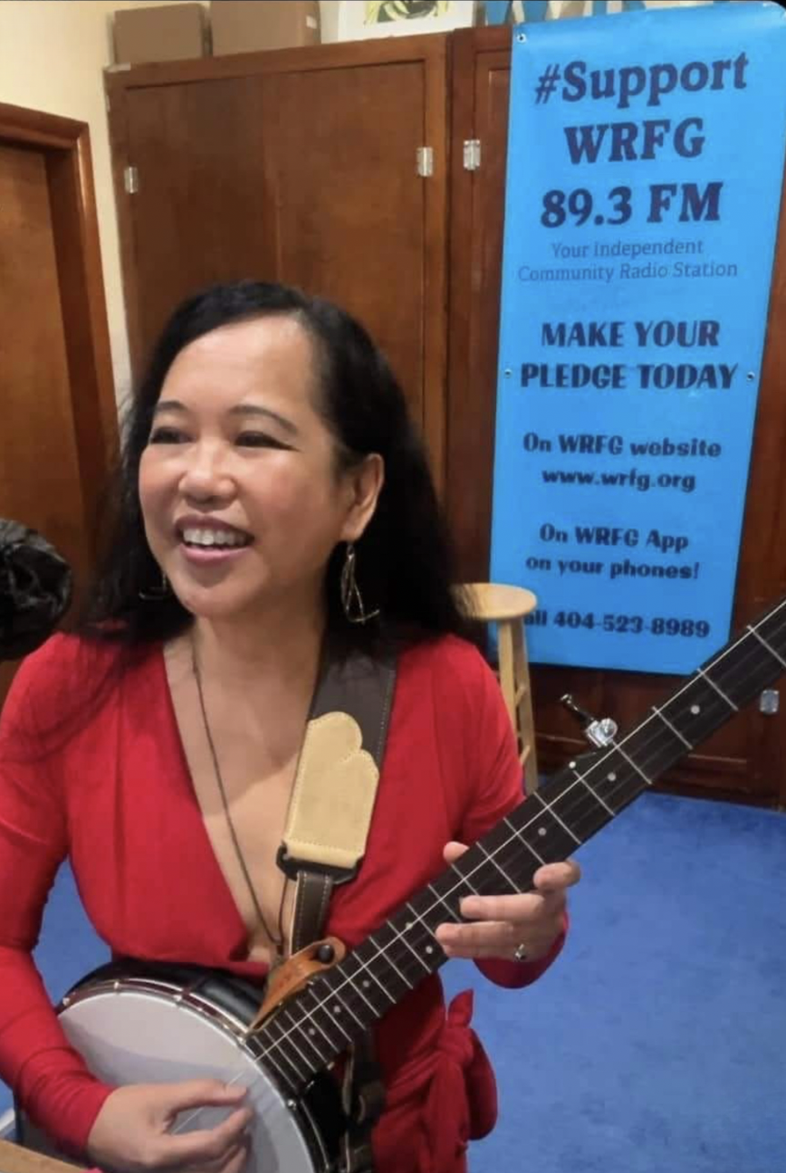 Silvia Passiflora, Southern Gothic Folk poet-songwriter, smiling while holding her banjo at WRFG 89.3 FM, Atlanta's independent community radio station.