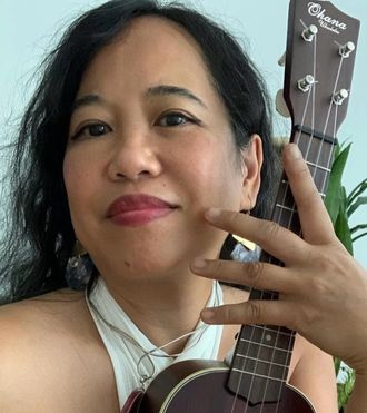 Silvia Passiflora, Southern Gothic Folk poet-songwriter, in a close portrait smiling warmly with her Ohana ukulele held close, captured in an informal moment between songs. 