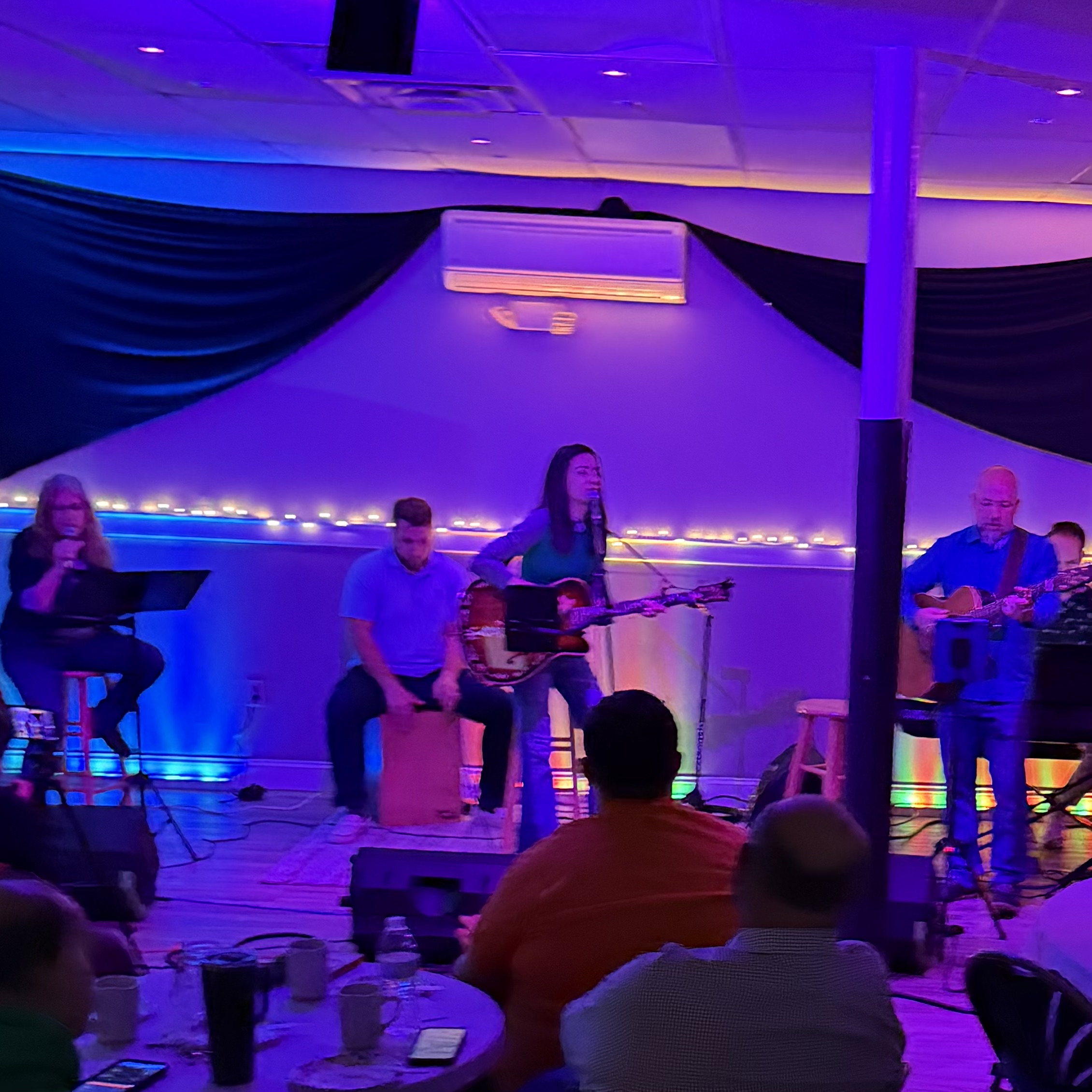 Laura Breece Band singing and playing, worshipping in a low lit room that is filled with people at tables.