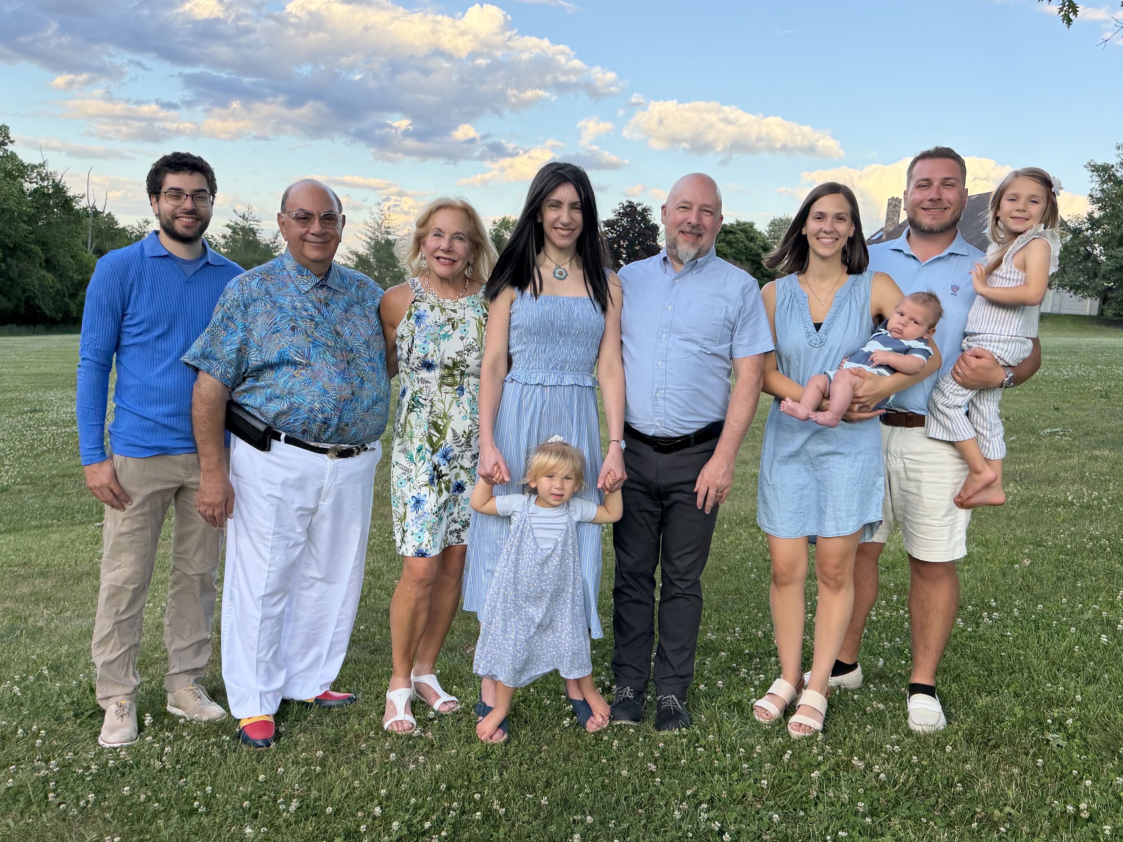A Photo of a flower littered grassy yard, a beautiful puffy clouded sky with Laura and her family
