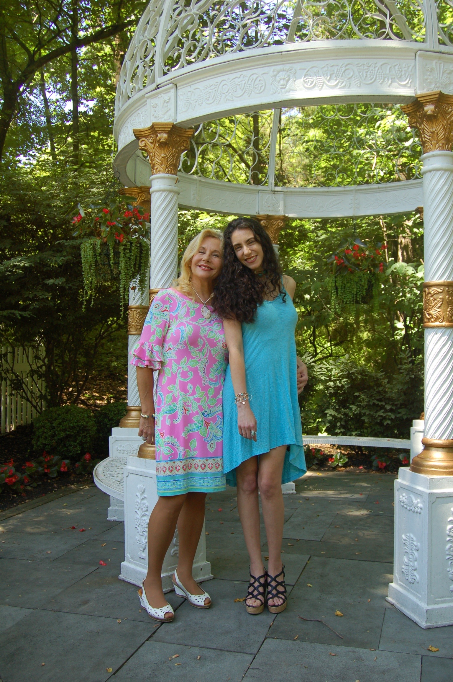 Photo of Laura who has brown curly shoulder length hair and her mom who has blond shoulder length hair.  They are wearing dresses and have matching light blue.  They are smiling happily.