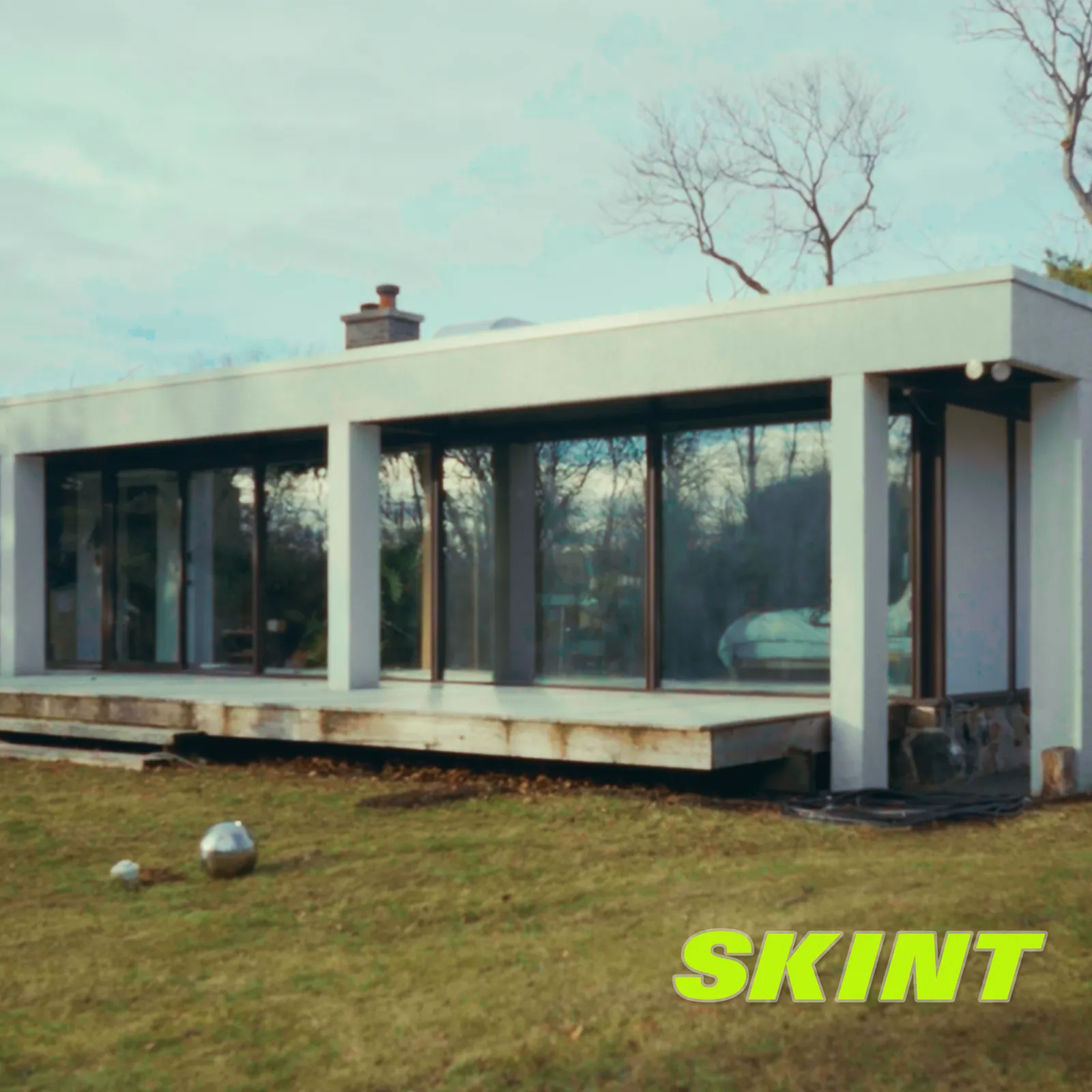 Skint single artwork: a flat-roofed glass house on a winter lawn