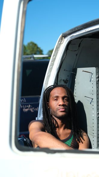 Jamaican artist EmE leaning from a vintage vehicle window in an outdoor portrait