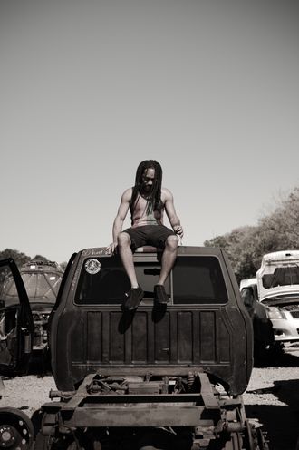 Jamaican artist EmE seated on a vintage vehicle during an outdoor photo shoot