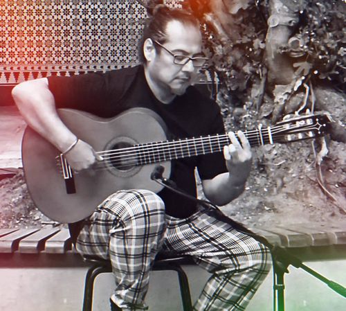 Shane playing his guitar in outdoor patio, poetry slam Malaka