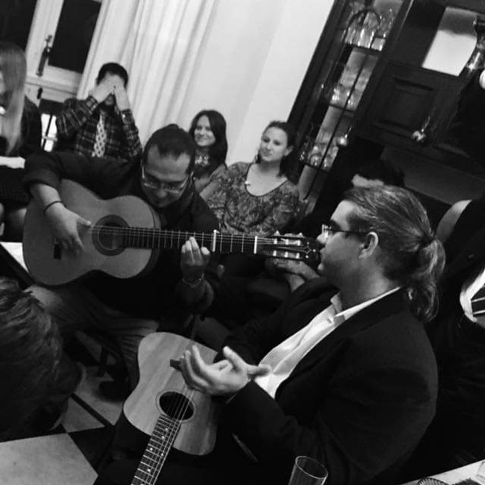 Shane Gonzalez and friends enthusiastically strumming guitars in a warm, inviting room filled with music.
