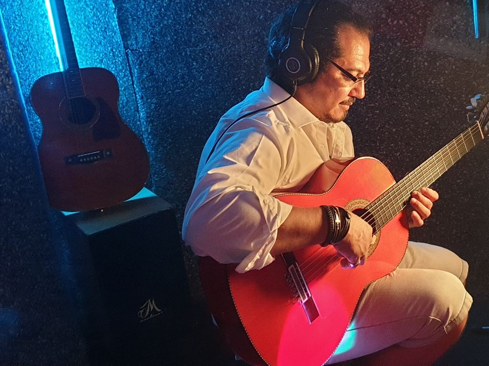 Shane Gonzalez passionately plays an acoustic guitar in a dynamic recording studio filled with instruments and sound equipment.