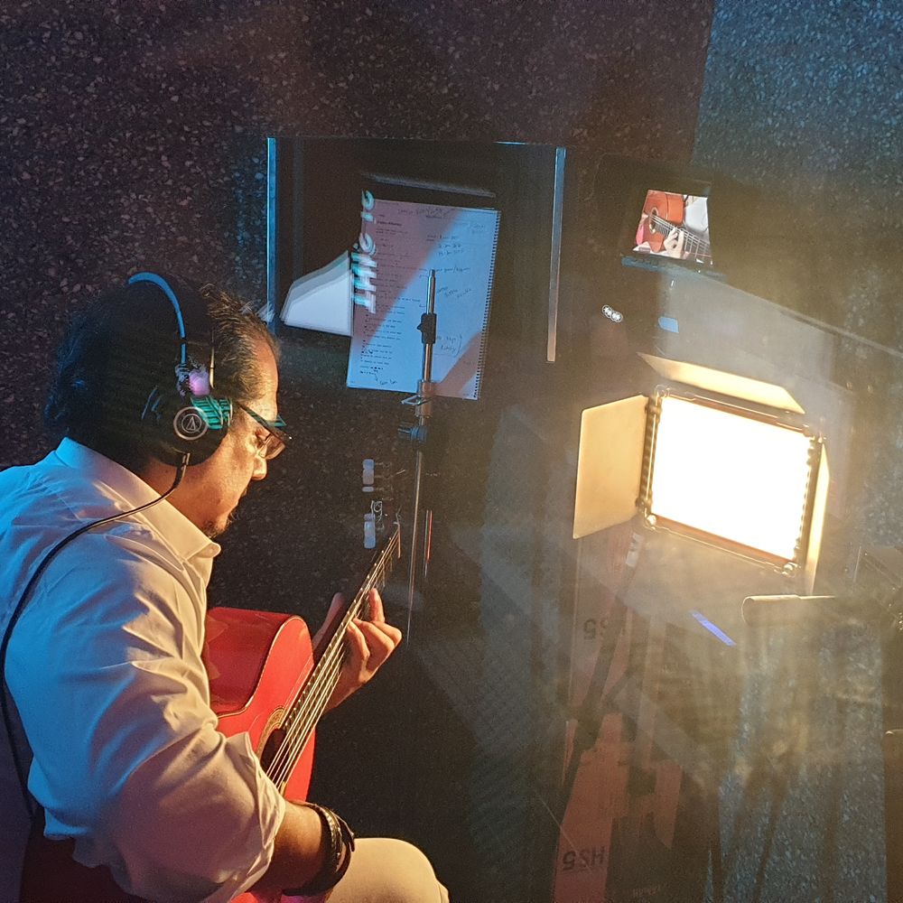 Shane Gonzalez passionately plays guitar in his recording studio, with a screen displaying his creative process nearby.