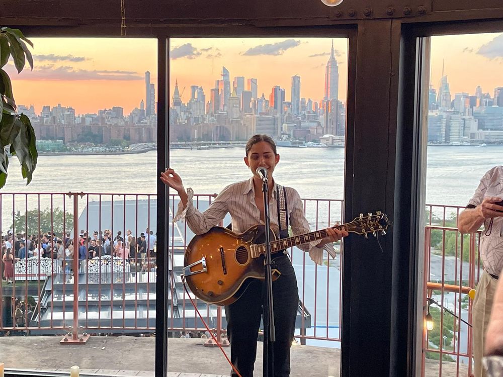 Dida Pelled performing live with guitar at a private event in New York at sunset, elegant ceremony music with Manhattan skyline in the background.