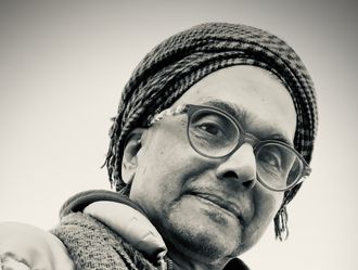 Black and white image of Ignatius in a head wrap, looking down as the camera looks up.