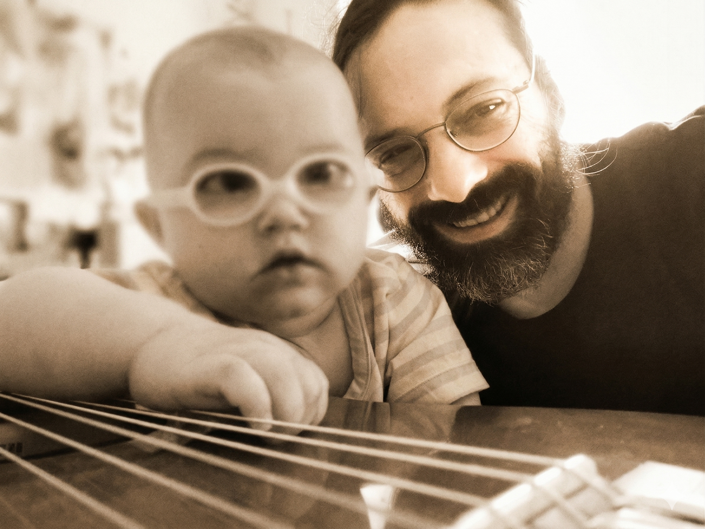 Persönlicher Moment: Musiker Andy Wilsing beobachtet lächelnd seine einjährige Tochter mit Brille, wie sie neugierig die Saiten seiner Gitarre erkundet