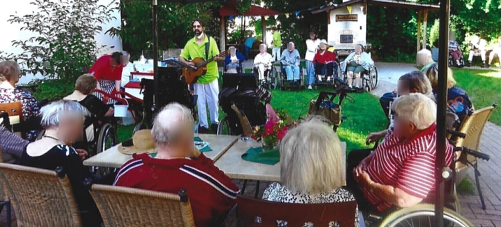 Musiker und Betreuer Andy Wilsing spielt Gitarre für Senioren im Garten einer Pflegeeinrichtung – Singrunde mit pflegebedürftigen Menschen.