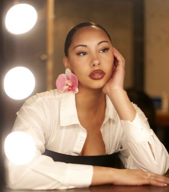 Madison Rose as Sade, looking into retro mirror with pink orchid earrings