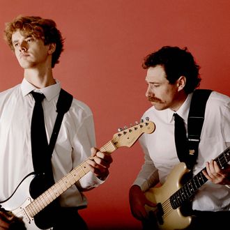 Guitarist and bassist performing together against a vibrant red background