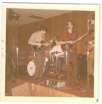 Tom Schizzano sitting in at the Moose Hall, Spring 1970 Tom played in a band called "Orange Cross" at this time, but sat in with us on this gig. I don't think the 'tards minded too much. He was (and is) a phenomonal musician who played keyboards as well as guitar and sang like an angel. I'm pretty sure he brought down the horn you can see in the left corner. Adding a horn to our PA system at that time was like adding primary colors to a palette of brown and grey. The box in the lower left was a strobe light that I built from an old window fan. Or maybe it was a monitor that Tom brought as well, in which case he got massive cred for upgrading our Bogen-powered PA a hundredfold. Ominous portents of the future: Tom now runs Landford Productions, one of Long Island's biggest recording studios, and David Meyer became a sales rep for Bogen amplifiers. Left to right: Tom Schizzano on black Les Paul; Scott Kistenberger on drum batterie, moi on cherry SG; David Meyer as Mr. Tambourine Man.
