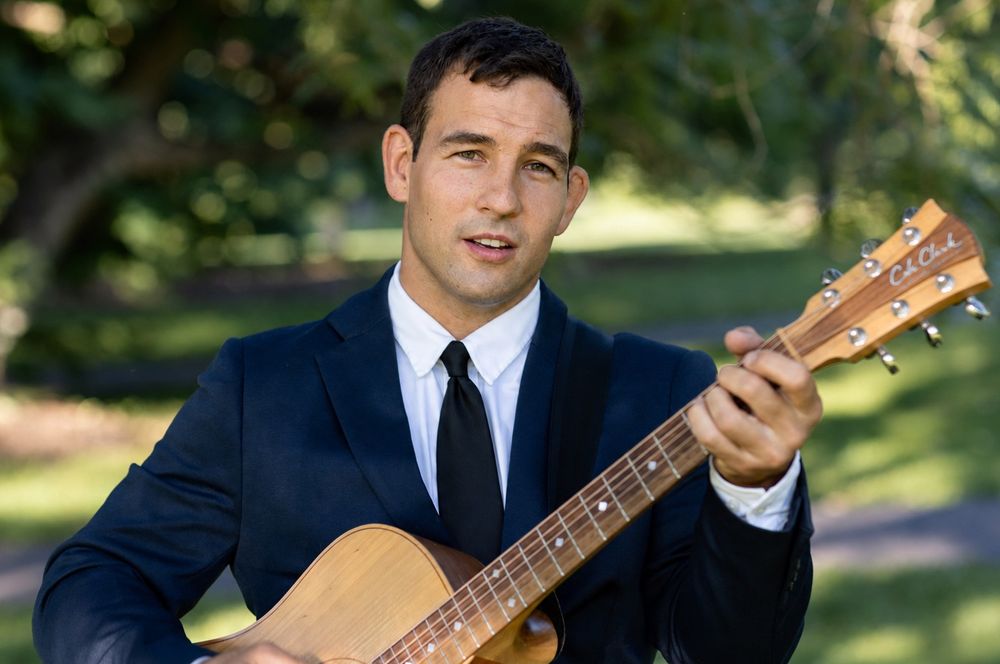 Johnny Walylko playing acoustic guitar in a suit outdoors.