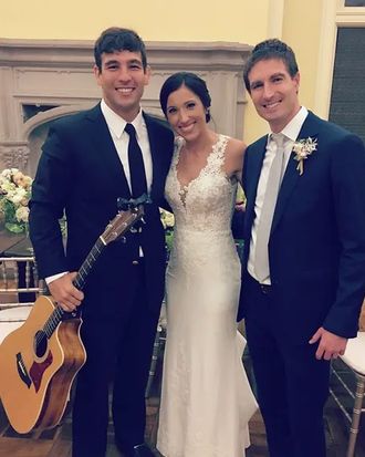 Johnny Walylko holding an acoustic guitar beside a bride and groom after their wedding.