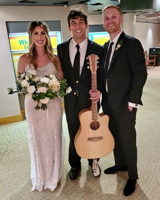Wedding singer Johnny Walylko posing with a bride and groom while holding his acoustic guitar.