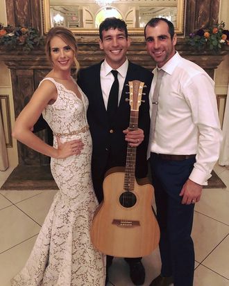 Johnny Walylko with his acoustic guitar alongside a bride and wedding guest at a reception.
