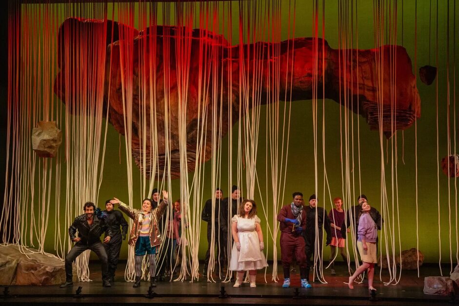 The cast beneath a red stone form and curtains of pale strings