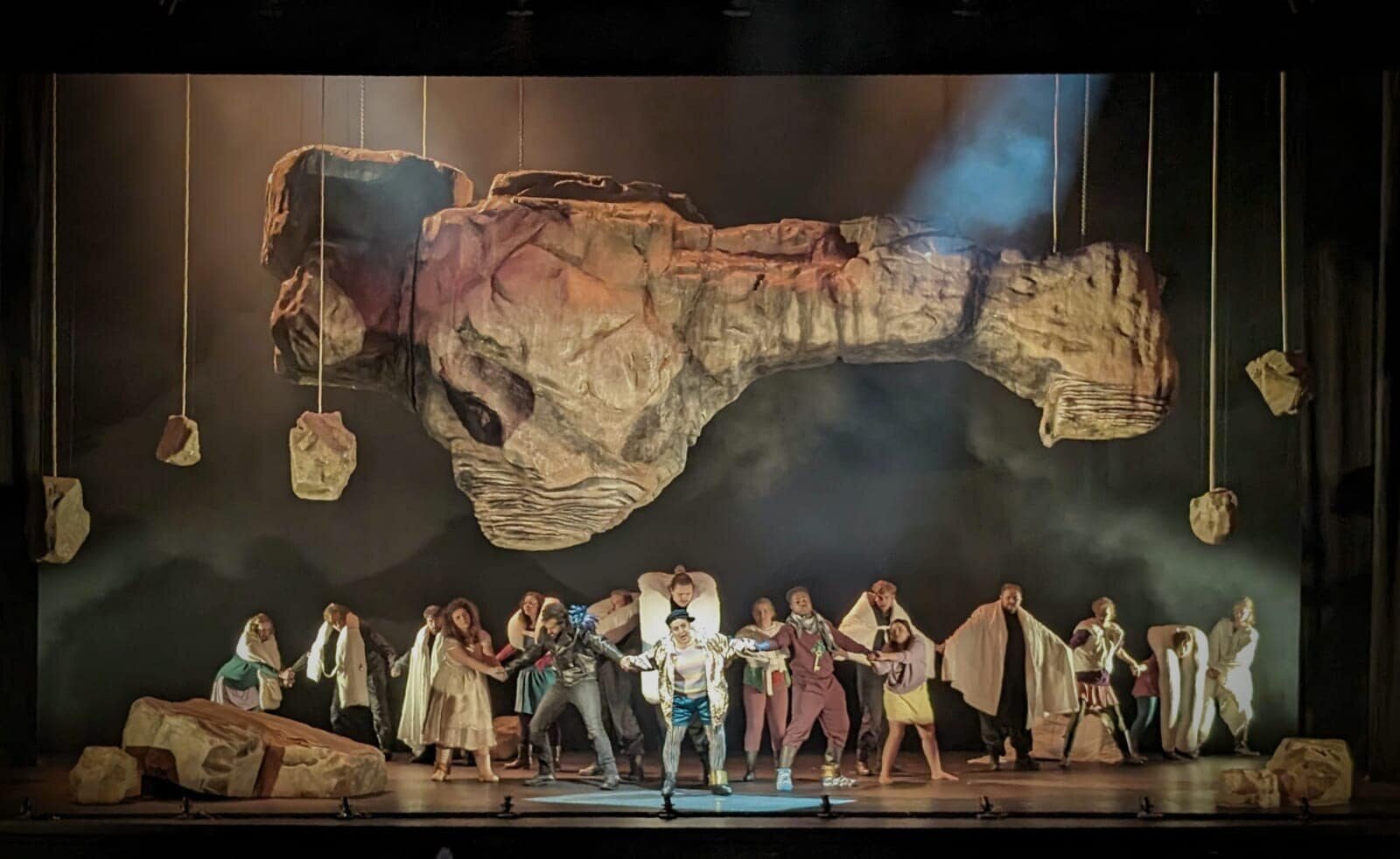 The chorus in pale cloaks beneath a vast suspended stone