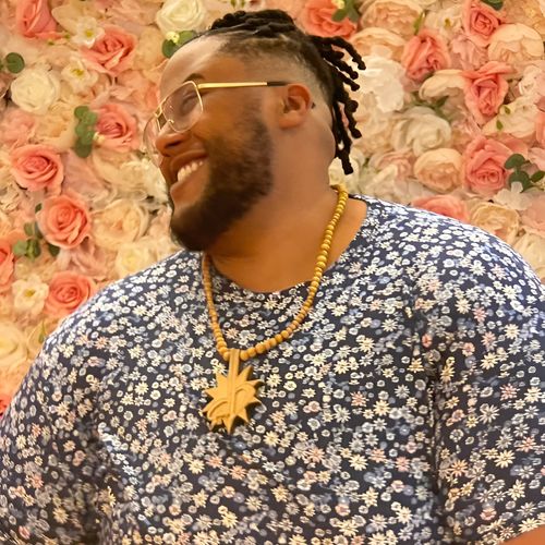 David TV Barnes in a floral shirt with a gold chain against a flower wall